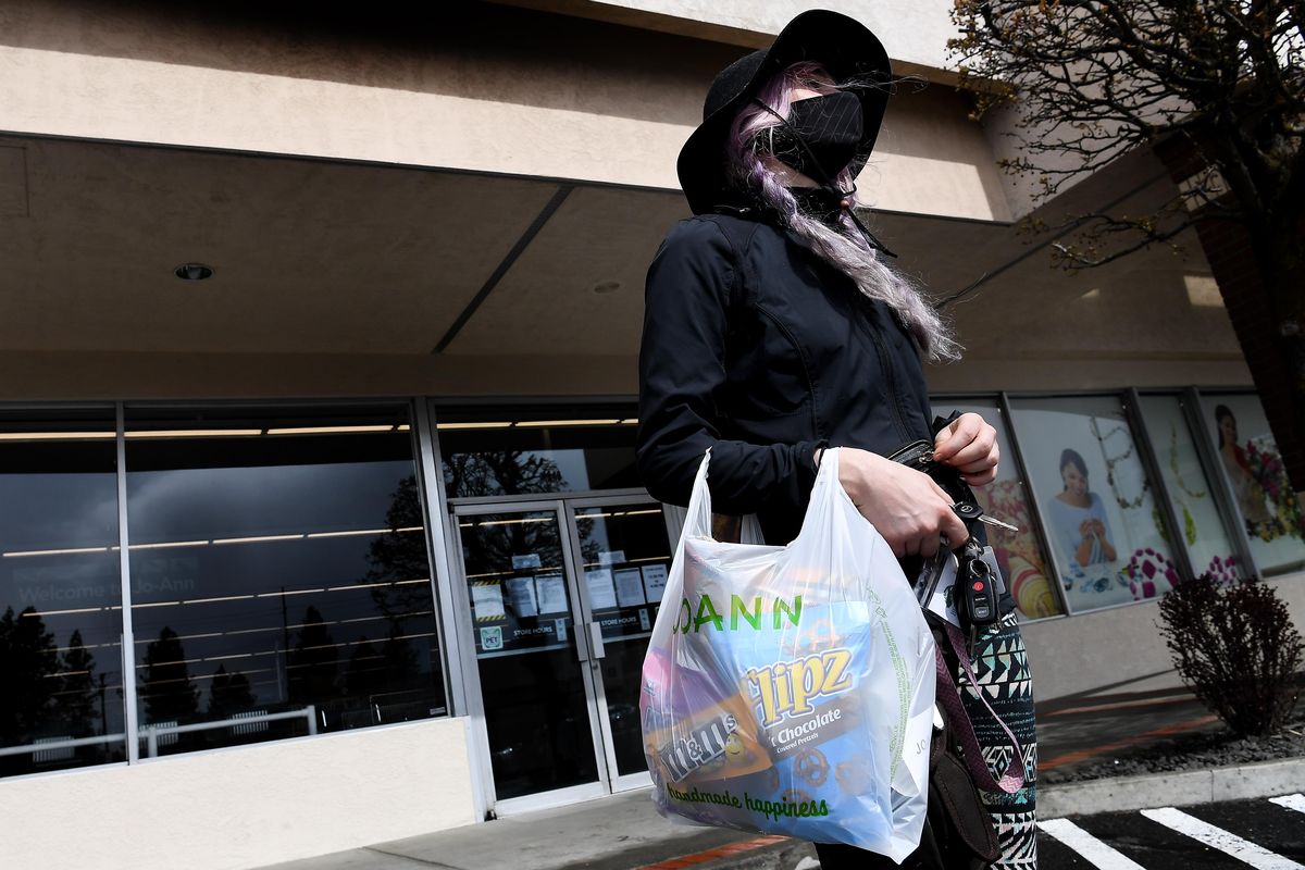 Allison Tripp, 28, carries supplies out of JOANN Fabrics and Crafts on March 29 in Spokane. A directive issued Wednesday requires all residents to wear face coverings at indoor or confined public settings when they will be within six feet of another person whom they don’t live with. (Tyler Tjomsland / The Spokesman-Review)