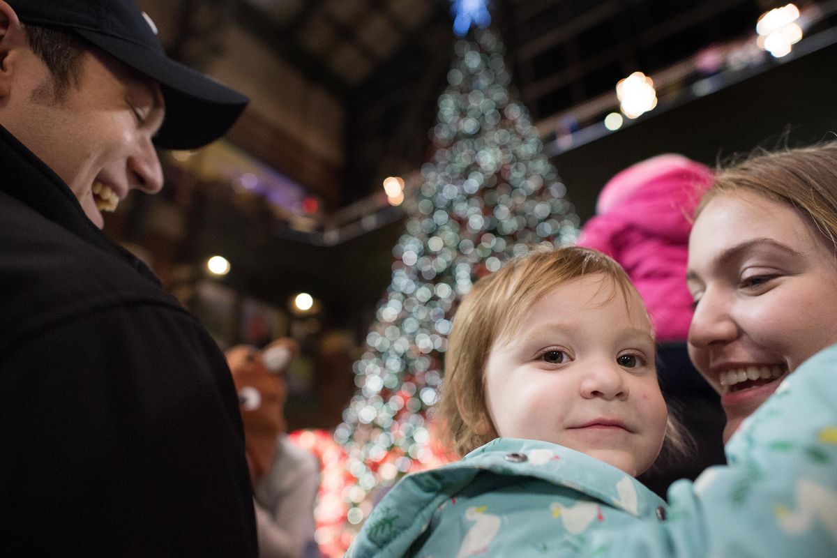 Samantha Terrell, holds her daughter Elliena, 2, as her father and Terrell’s fiancé, Adam Lague, left, smiles during a Christmas tree lighting on Friday, Nov. 17, 2017, at River Park Square in Spokane, Wash. (Tyler Tjomsland / The Spokesman-Review)