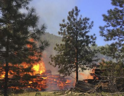 In this May 23, 2017, photo provided by Chelan County Fire District 3, a pile of logs burns near Leavenworth, Wash. The wildfire that started at an old log-storage site has prompted evacuation orders for homes and cabins at a popular Washington state hiking and skiing destination, officials said Wednesday. (Ben Torkelson / Ben Torkelson/Chelan County Fire District 3)