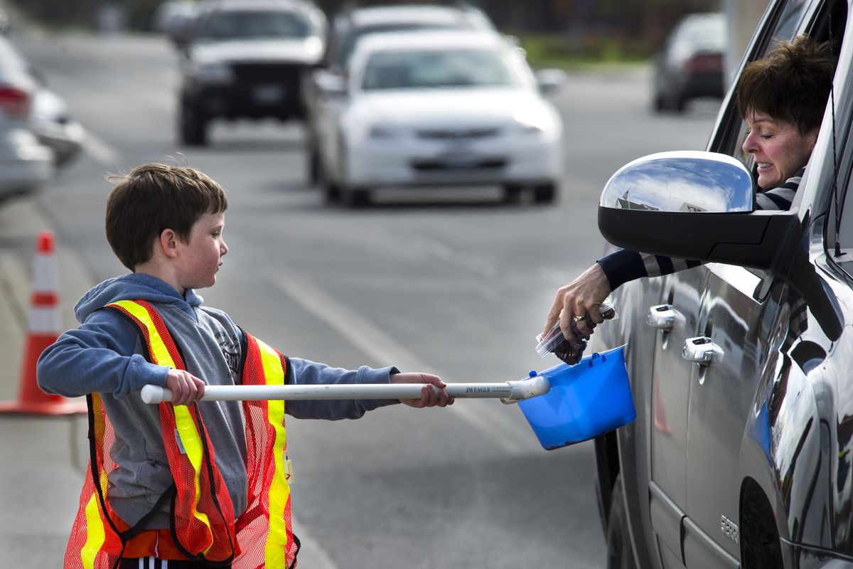 Cole Conway, 7, receives a bag of coins from a motorist near the corner of East 57th Avenue and South Regal Street on Saturday, during the Spokane Guilds’ School’s 18th annual Kids for Kids Penny Drive. Cole’s younger brother, James, is a Guilds’ School graduate. (Dan Pelle)