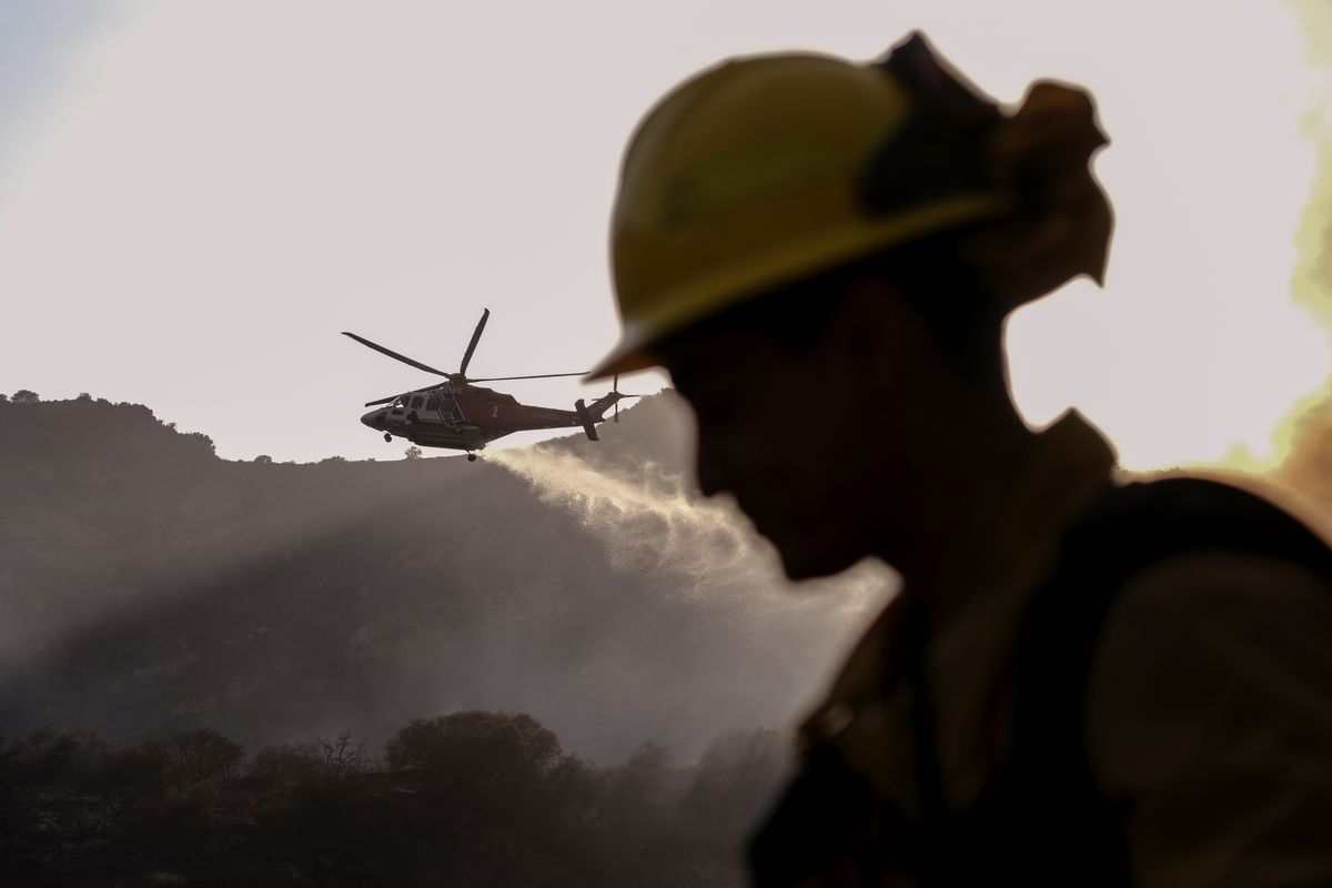 A firefighter keeps watch as a firefighting helicopter drops water on a brush fire scorching at least 100 acres in the Pacific Palisades area of Los Angeles on Saturday, May 15, 2021.  (Ringo H.W. Chiu)