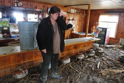 Linda Mitchell, owner of the Roadside Inn Tavern in Glenoma, Wash., stands in shock Friday after describing her rescue from a mudslide with the help  of a friend with an excavator and her yellow Lab. She made it out alive but her home and tavern are under 4 feet  of mud.  (Associated Press / The Spokesman-Review)