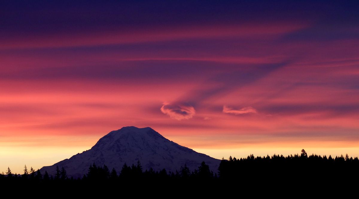 Low lying clouds cast shadows on the higher cloud ceiling as as the sun rises behind Mount Ranier, Washington’s iconic peak, in January 2012. (Steve Zugschwerdt / File/Associated Press)