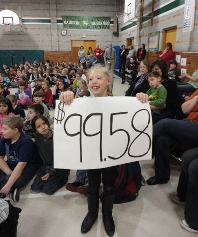 Mia Roberts, a student in teacher Amanda Workman’s class at Madison Elementary School, holds up a sign indicating the $99.58 her class raised in a change drive to benefit classmate Snezhana Dedkov.