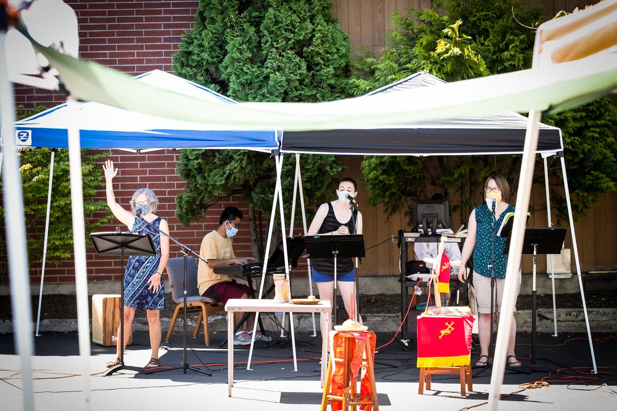 Framed by canopies, from left: Shadle Park Presbyterian Elder of Adult Discipleship Bonnie Hansen, Asst. Family Ministries Director Courtney Durrant and Associate Pastor Alyssa Bell sing to close the Sunday service on Aug. 2, 2020 in the parking lot of the church in Spokane, Wash during the COVID-19 pandemic. Strict social distancing measures were enforced for in-person members, including mandatory masks, spaced out seating, prepackaged communion and no sharing of materials for the service that was presided over by Associate Pastor Matthew Bell. At-home worship was also available through a livestream for those that didn