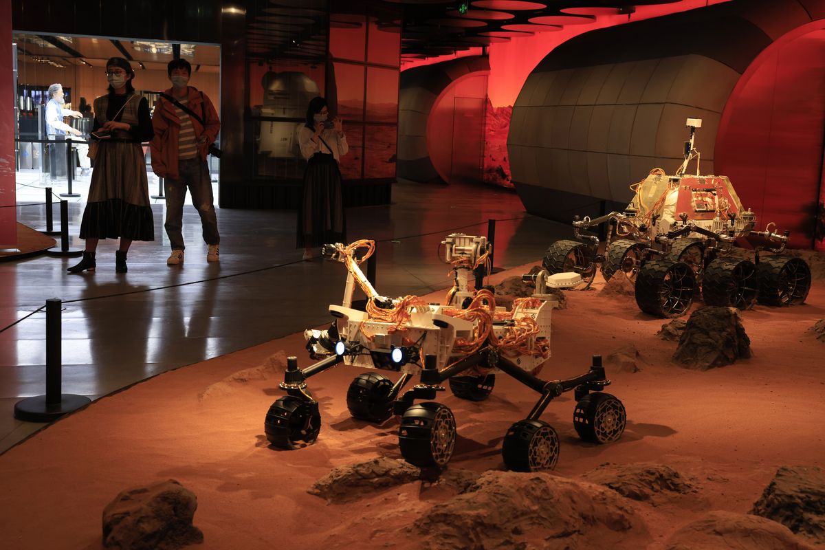 Visitors pass by an exhibition depicting rovers on Mars in Beijing on Friday, May 14, 2021. China says its Mars probe and accompanying rover are to land on the red planet sometime between early Saturday morning and Wednesday Beijing time.  (Ng Han Guan)