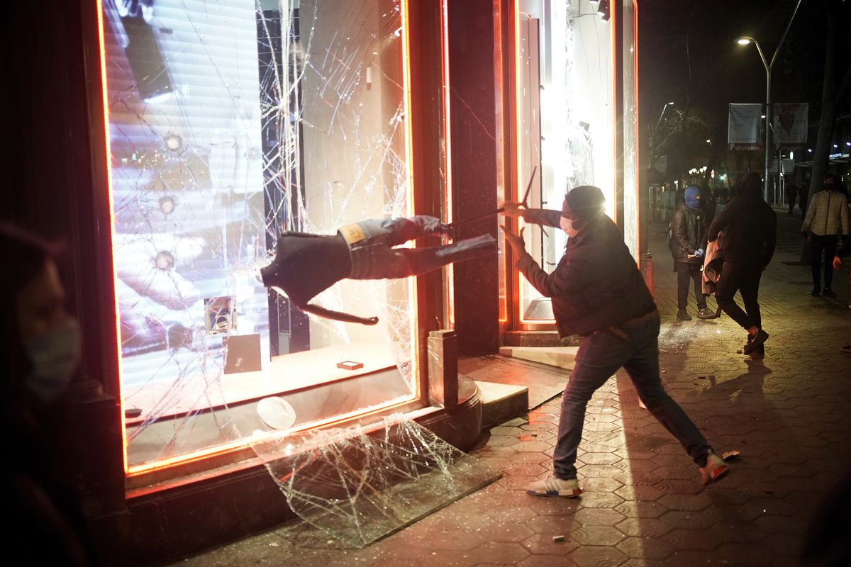 A demonstrator smashes a shop window during a protest condemning the arrest of rap singer Pablo Hasél in Barcelona, Spain, Saturday, Feb. 20, 2021. A fifth night of peaceful protests to denounce the imprisonment of a Spanish rap artist once more devolved into clashes between police and fringe group members who set up street barricades and smashed storefront windows in Barcelona.  (Joan Mateu)