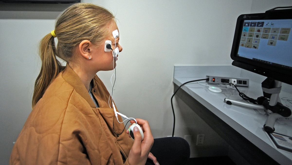 Sacajawea Middle School student Anna Ashenbrener is outfitted with sensors on her face, Thursday, April 14, 2022. Sacajawea teacher Kim Taylor brought her STEM engineering class to the Steve Gleason Institute of Neuroscience to have hands on experience in adaptive technology for those with physical disadvantages. Ashenbrennerl is learning to use her facial muscles to remotely control the computer at far right.   (Christopher Anderson/For The Spokesman-Review)