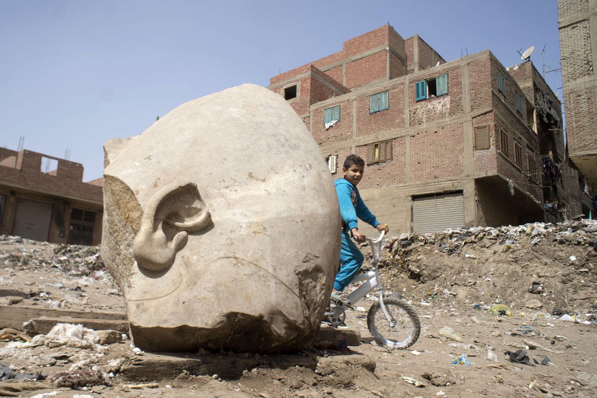 A boy rides his his bicycle past a recently discovered statue in a Cairo slum that may be of Pharaoh Ramses II, in Cairo, Egypt, Friday, March 10, 2017. Archeologists in Egypt have discovered a massive statue that may be of Ramses II, one of the country’s most famous ancient rulers. The colossus, whose head was pulled from mud and groundwater by a bulldozer on Thursday, is around eight yards tall and was discovered by a German-Egyptian team. (Amr Nabil / Associated Press)