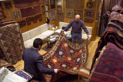 
 Erol Kazanci, back, owner of Gallery Shirvan, and Mustafa Yilmaz examine a rare 19th century pinwheel Kazak rug in Istanbul, Turkey. 
 (Knight Ridder / The Spokesman-Review)