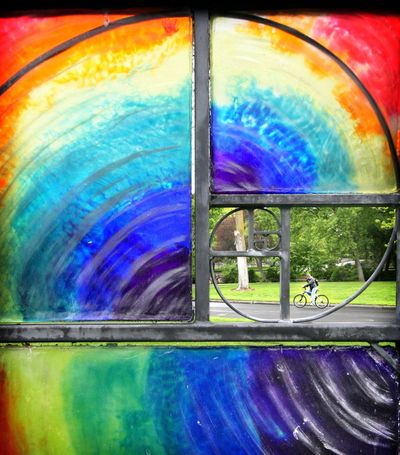 Color wheel: Framed within the swirling rainbow colors of a glass and welded steel sculpture on the Whitman College campus, a lone bicyclist pedals through rainy streets of Walla Walla on Tuesday. The art piece, “Imagination and Understanding: Phusis and Techne,” is an outdoor work by artist Doug Ludlow and has been on the campus grounds since 2001. (Associated Press)