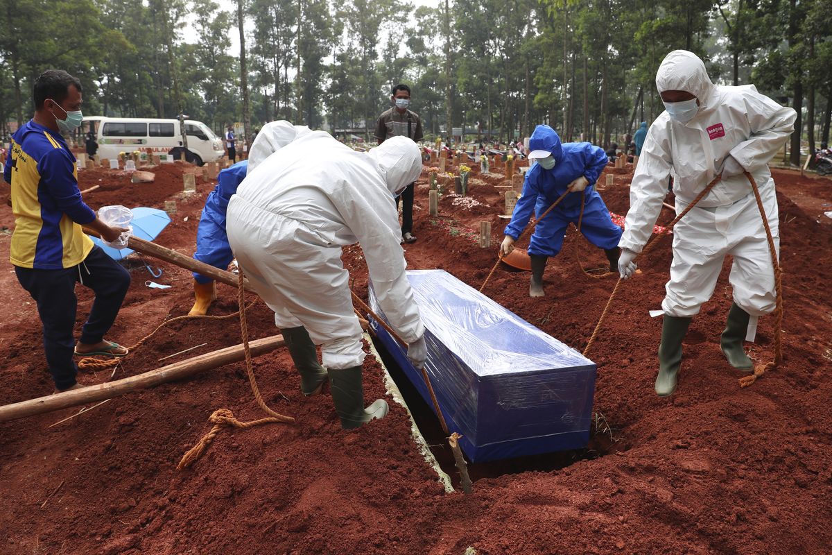 Workers in protective gear lower a coffin of a COVID-19 victim to a grave for burial at the Cipenjo Cemetery in Bogor, West Java, Indonesia, Wednesday, July 14, 2021. The world’s fourth most populous country has been hit hard by an explosion of COVID-19 cases that have strained hospitals on the main island of Java.  (Achmad Ibrahim)