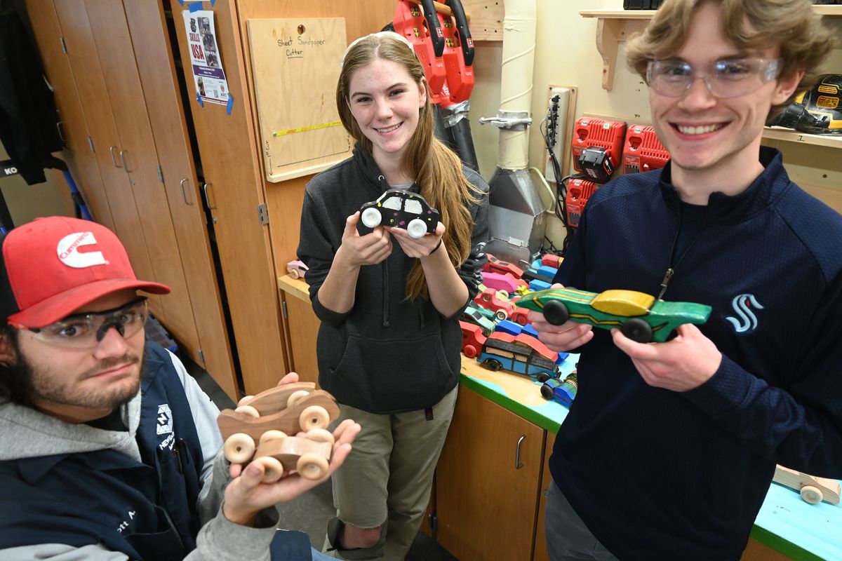 Ferris High School wood shop students Elliott Attrill, left, Iza Maselko and Owen Fassbender hold some of the dozens of wooden cars built in the wood shop class Tuesday at Ferris and painted by art classes down the hall.  (Jesse Tinsley/The Spokesman-Review)