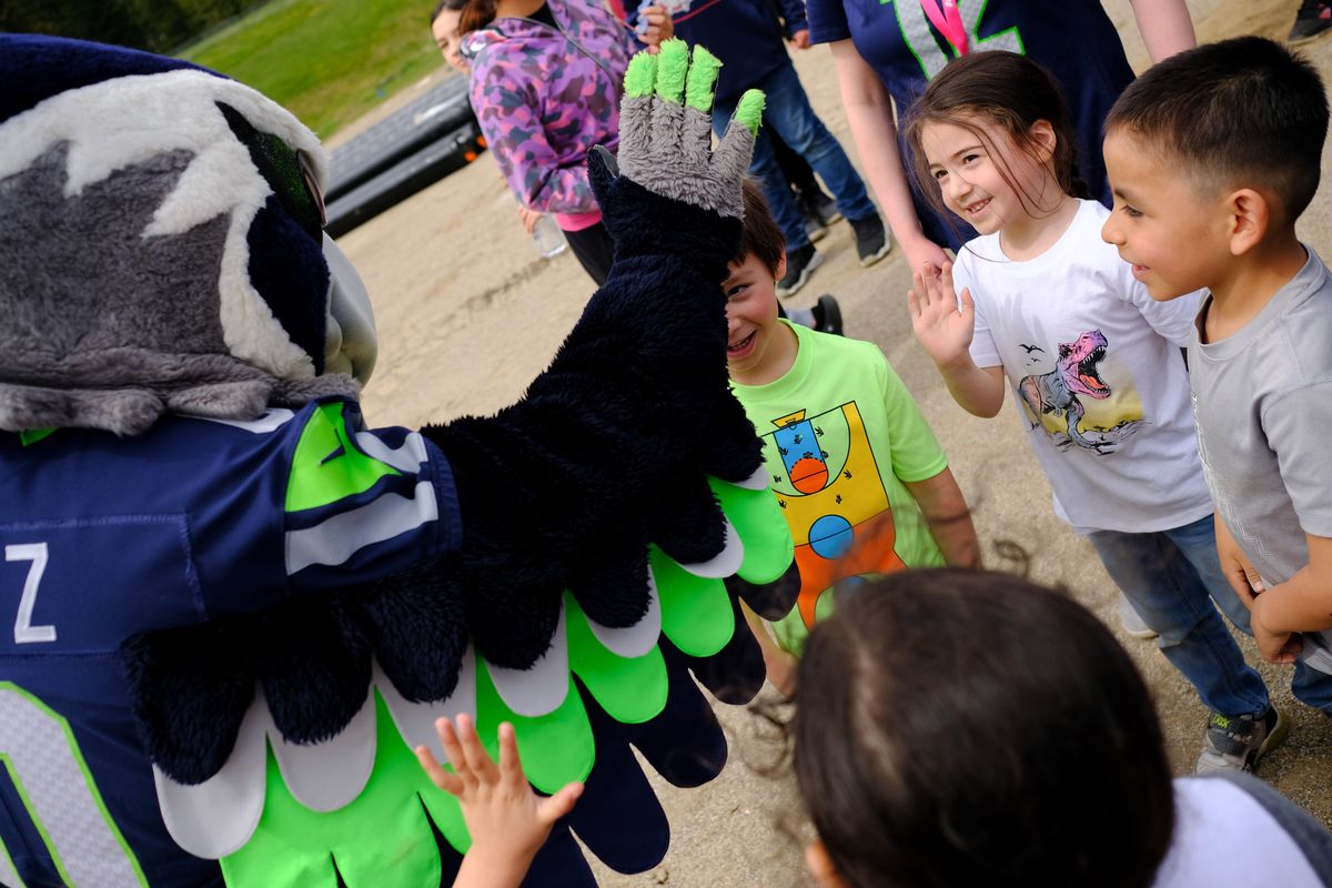 Kindergartner Grayson Wynecoop, right, in t-rex shirt, smiles before grabbing a high-five from Seahawks mascot Blitz after a groundbreaking ceremony for a new football field on Wednesday, May 4, 2022, at Wellpinit High School in Wellpinit, Wash.  (Tyler Tjomsland/The Spokesman-Review)