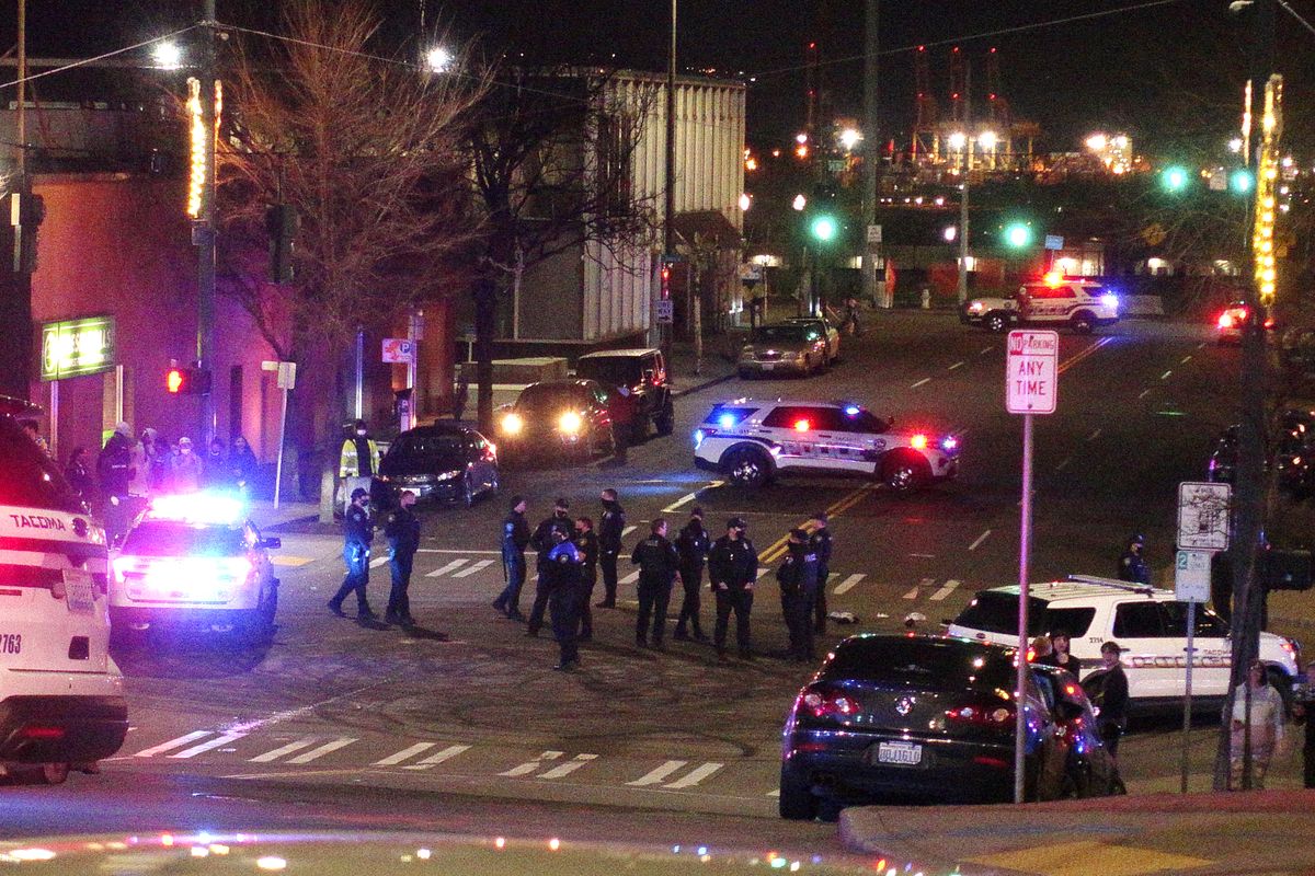 Tacoma Police and other law enforcement officers stand in an intersection near the site of a car crash Saturday, Jan. 23, 2021, in downtown Tacoma, Wash. At least one person was injured when a police car plowed through a crowd of people Saturday night who were watching a downtown street race, the Tacoma News-Tribune reported.  (Ted S. Warren)