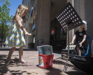 Aria Sing, 4, of Sandpoint, Idaho, donates a dollar bill into the buck of musicians Ivy, Neilia and Carey Eyer, during Street Music Week, June 2, 2017, in downtown Spokane, Wash. (Dan Pelle / The Spokesman-Review)