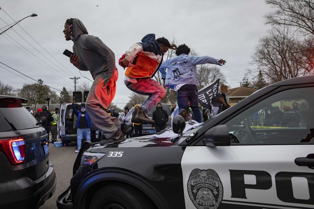 Men jump on the hood of a police car after a family said a man was shot and killed by law enforcement on Sunday, April 11, 2021, in Brooklyn Center, Minn.  (Christian Monterrosa)
