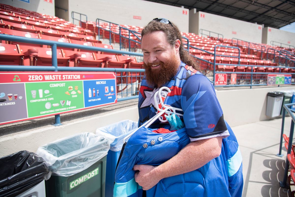 Brad Bishop carries the costume of RecycleMan, a mascot character he has played for more than 12 years at Spokane Indians baseball games. He is stepping away from his mascot job because his day job. working in the mental health field, is demanding more and more of his time. Photographed Thursday, July 7, 2022 at Avista Stadium. He paused here to point out the recycling baskets inside the stadium, where he often stops to interact with fans.  (Jesse Tinsley/THE SPOKESMAN-REVI)
