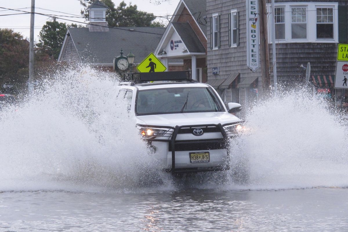 This Oct. 11, 2019 photo shows a car kicking up spray while driving through a flooded street in Bay Head, N.J. New Jersey