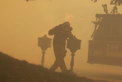 A Los Angeles firefighter heads for the cover of a fire engine while flames burn near homes in Los Angeles’ Granada Hills area.  (Associated Press / The Spokesman-Review)