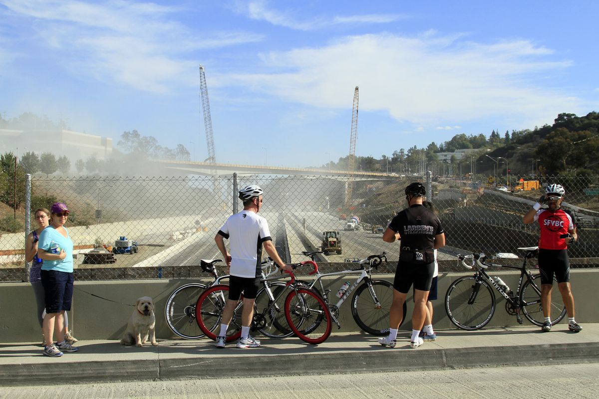 Morning walkers and bicyclists stop on Skirball Bridge to view and photograph heavy equipment busy in the demolition of part of the Mullholland Drive bridge over the 405 freeway early Sept. 29, 2012 in Los Angeles. Construction crews began work early Saturday taking down a portion of the Mulholland Drive bridge along Interstate 405, one of the nation