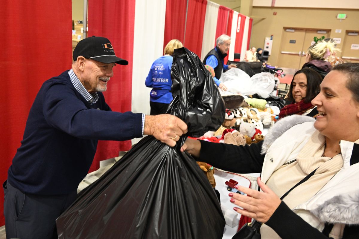 Volunteer Tim Welsh, left, hands a bag of toys and gifts to clients as they pass through the Christmas Bureau Tuesday, Dec. 16, 2025 at the Spokane County Fair and Expo Center. Welsh was one of the founders of Garco Construction, one of the region