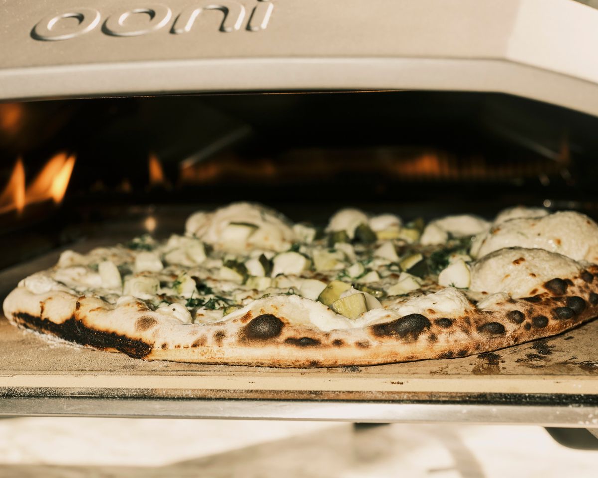A pickle-topped pizza cooks in a backyard pizza oven in Bradenton, Fla., on July 30. Tonio Viscusi of Angela’s Concessions, which sells food at fairs, said that over the years, he received dozens of requests from customers for a pickle pizza.  (Zack Wittman/The New York Times)