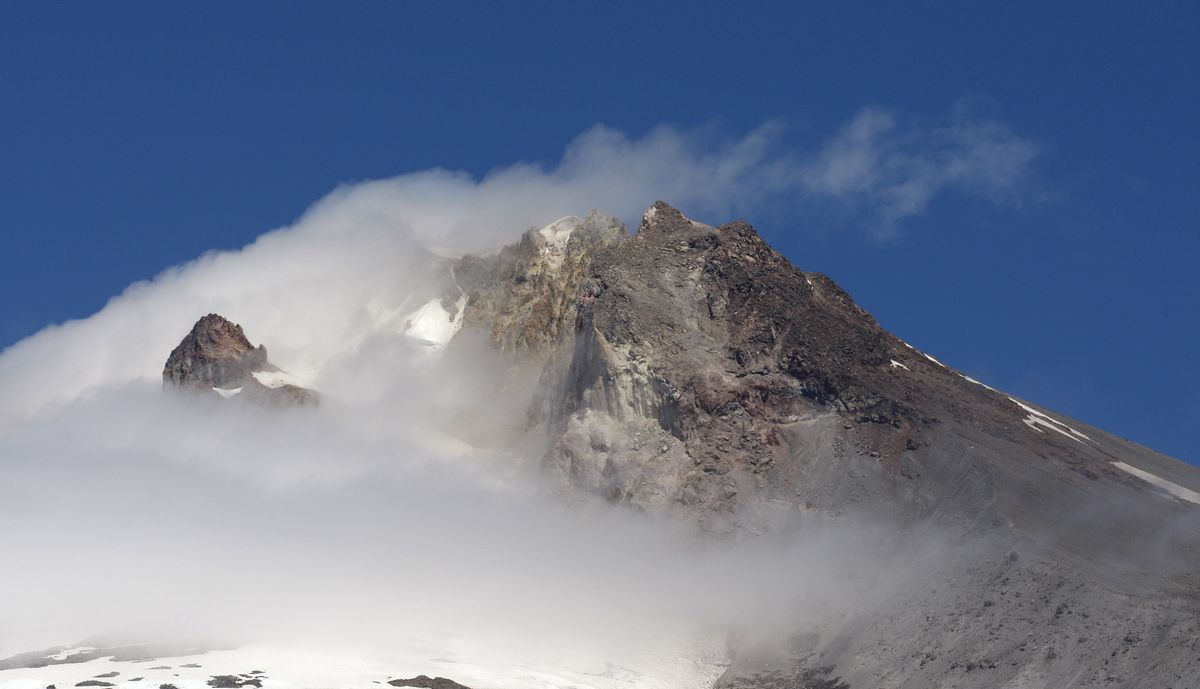 Mount Hood is seen  through  cloud cover Thursday. The remains of two climbers missing since December have been found near the summit.  (Associated Press)