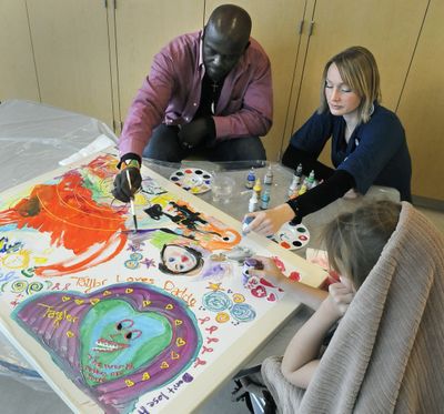 Nicholas Sironka, visiting artist and Ann Walker, Arts in Healing coordinator at Providence Sacred Heart Medical Center, work a on piece with a patient in the Children’s Hospital, Oct. 27.  (Dan Pelle)