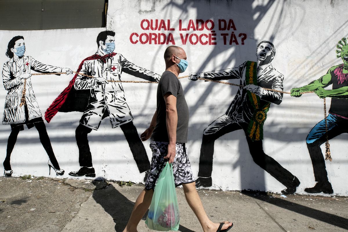 A man, wearing a protective face mask as a measure to curb the spread of the new coronavirus, walks past a mural depicting a tug-of-war between health workers and Brazil