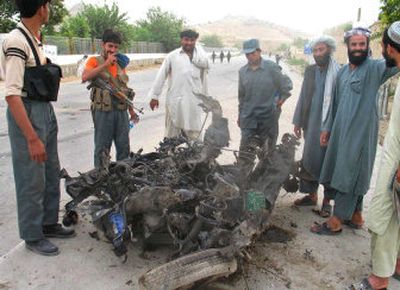 
Afghan police officers and others  look at the wreckage of a vehicle after a suicide car bombing killed at least 21 people in the Panjwayi district of Kandahar province, Afghanistan, on Thursday. 
 (Associated Press / The Spokesman-Review)