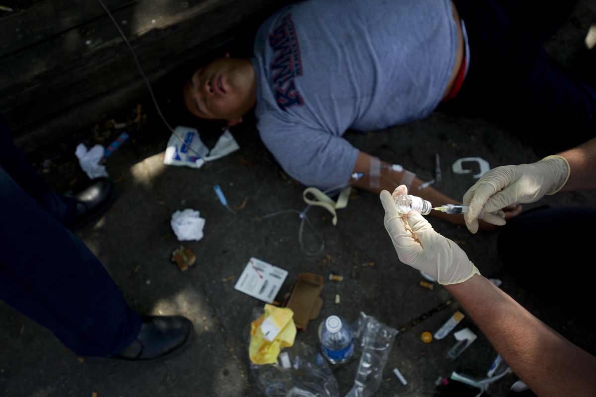 Brian Schaeffer, assistant chief of the Spokane Fire Department, right, prepares a needle while administering aid to an unconscious and apparently intoxicated man near Sprague Avenue and Browne Street in Spokane on Friday. (Tyler Tjomsland)