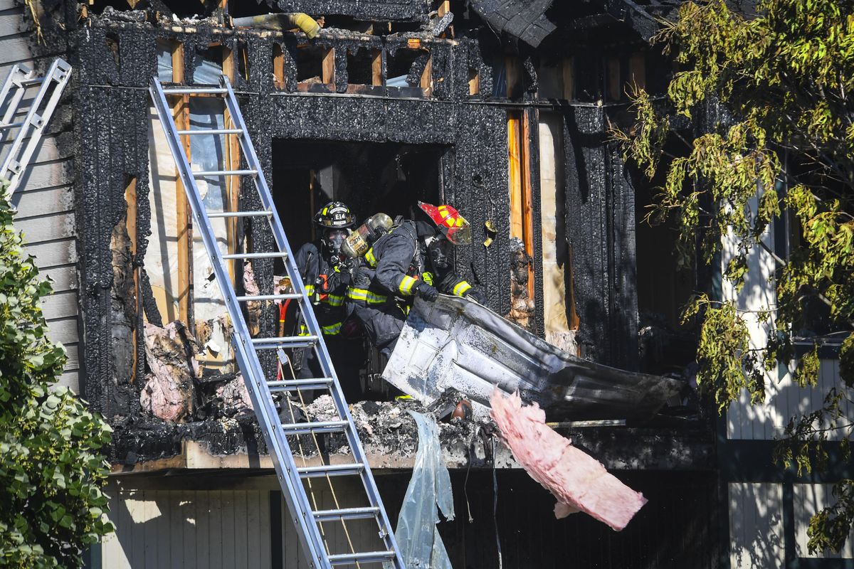 Spokane County Fire District 8 firefighters toss debris off the deck of a second-story Cedar Canyon Villas apartment that caught fire Thursday, August 2, 2018. (Dan Pelle / The Spokesman-Review)