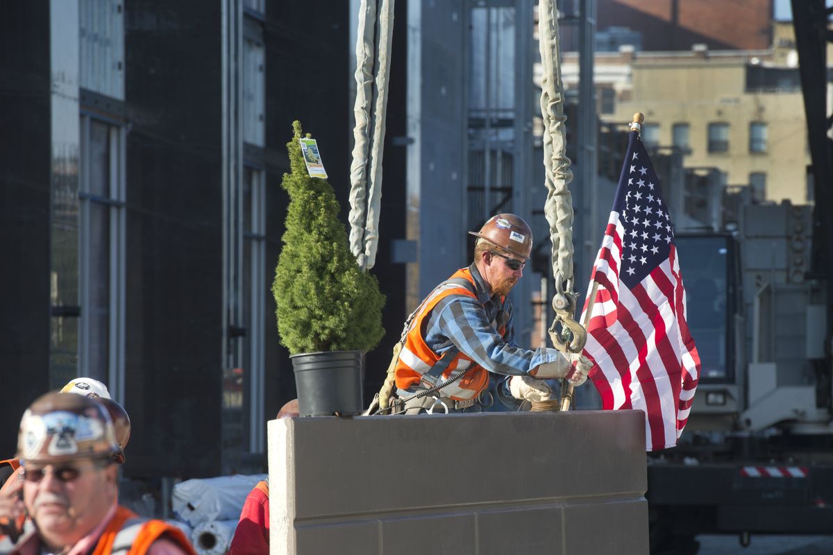 Ironworker Jason McDermott attaches an American flag, along with a small tree, to a final 7,000-pound panel to be raised into position atop the new Davenport Grand hotel in Spokane on Monday. Precision Precast Erectors co-owner Lou LaVe is at left. (Dan Pelle)