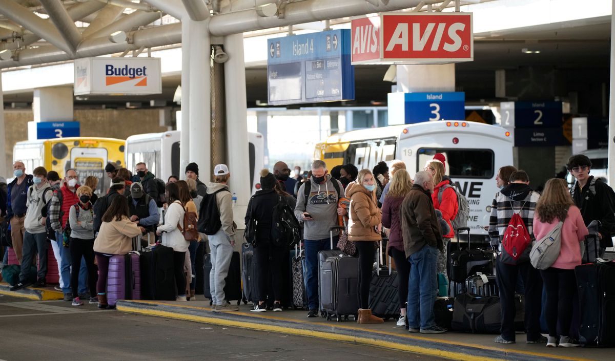 Travelers queue up for shuttle buses to renta car lots at Denver International Airport Sunday, Dec. 26, 2021, in Denver. Airlines cancelled hundreds of flights Sunday, citing staffing problems tied to COVID-19 to extend the nation