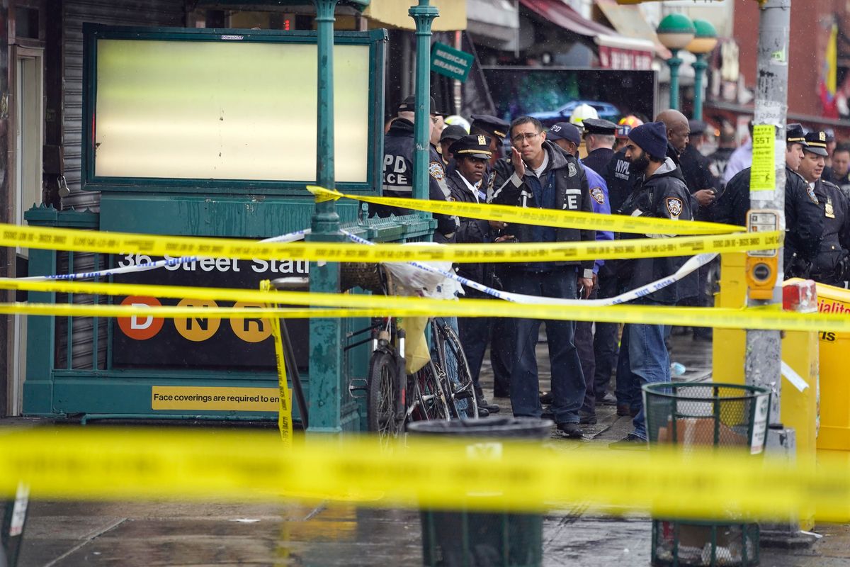 New York City Police Department personnel gather at the entrance to a subway stop in the Brooklyn borough of New York, Tuesday, April 12, 2022. Multiple people were shot and injured Tuesday at a subway station in New York City during a morning rush hour attack that left wounded commuters bleeding on a train platform.  (John Minchillo)
