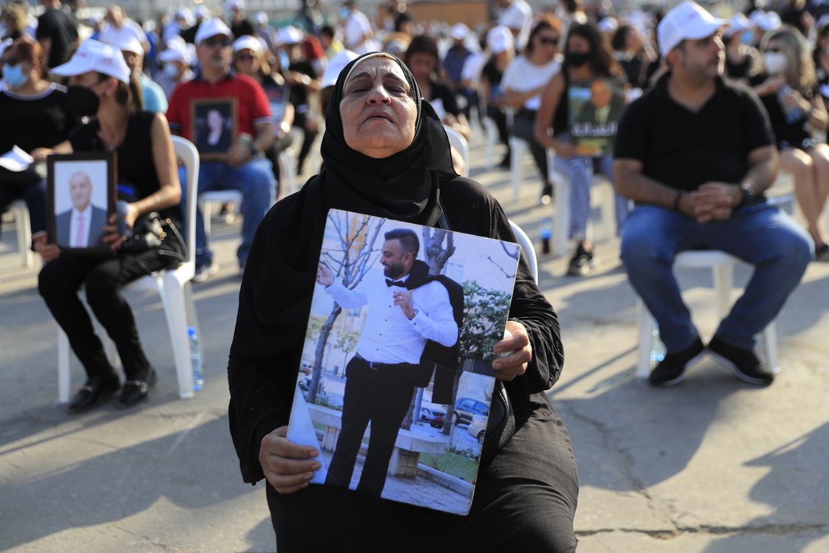 The mother of a victim who was killed in the massive blast last year at the Beirut port holds a portrait of her son as she attends a Mass held to commemorate the first year anniversary of the deadly blast, at the Beirut port, Lebanon, Wednesday, Aug. 4, 2021. United in grief and anger, families of the victims and other Lebanese came out into the streets of Beirut on Wednesday to demand accountability as banks, businesses and government offices shuttered to mark one year since the horrific explosion.  (Hussein Malla)