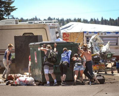 A group of people including Julie Garcia, of Jewels Helping Hands, third from left, help push the dumpster back into place at Camp Hope, homeless encampment in Spokane in this file photo from Thursday, July 14, 2022. A fence is going to be erected around the camp and an 8 p.m. curfew will be enforced.  (Kathy Plonka/The Spokesman-Review)