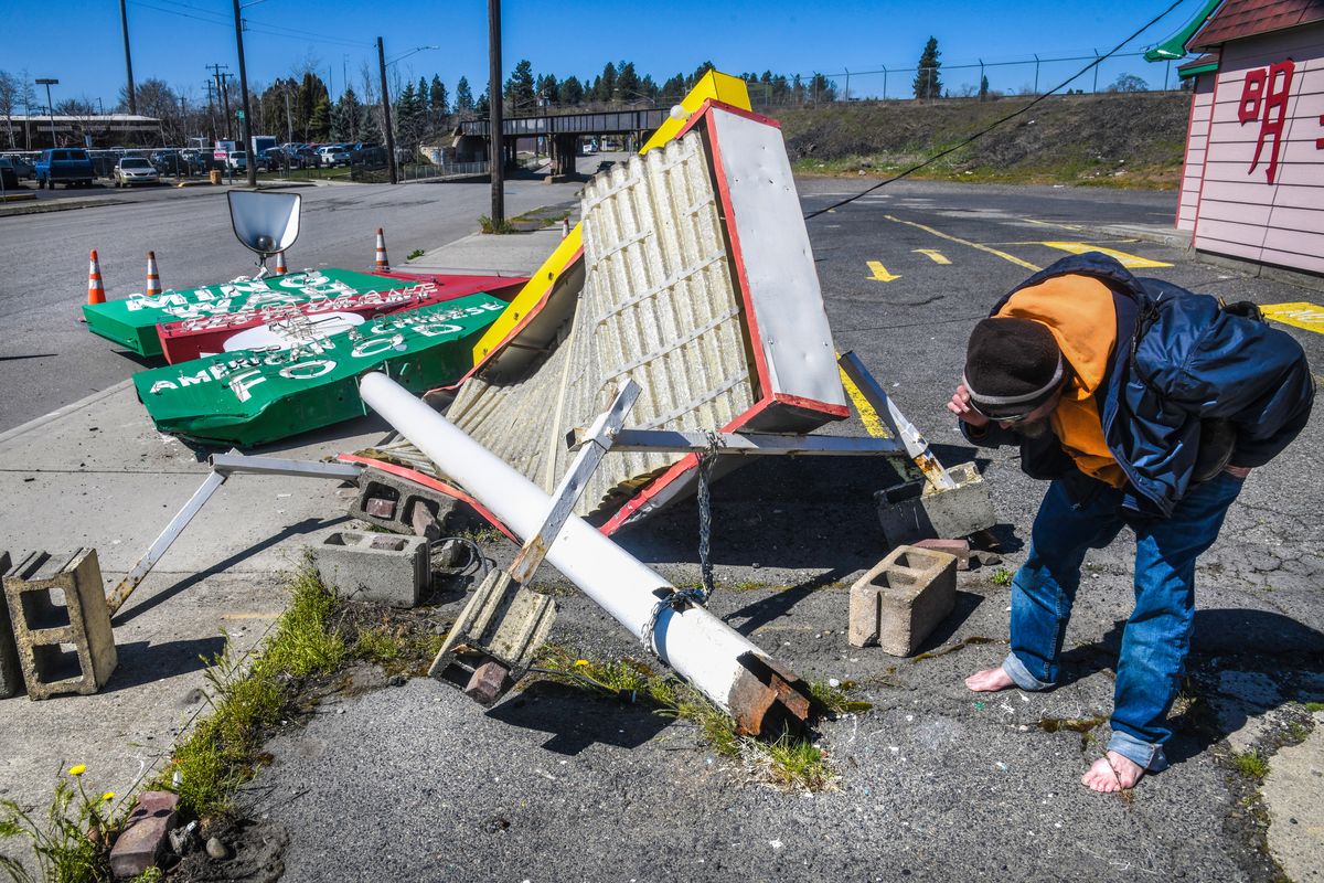 Passerby Jake Walsh, 47, gets a closer look at the rusted base of the fallen Ming Wah restaurant sign on April 1, 2020, near the corner of Third Avenue and Maple Street in downtown Spokane.  (DAN PELLE)