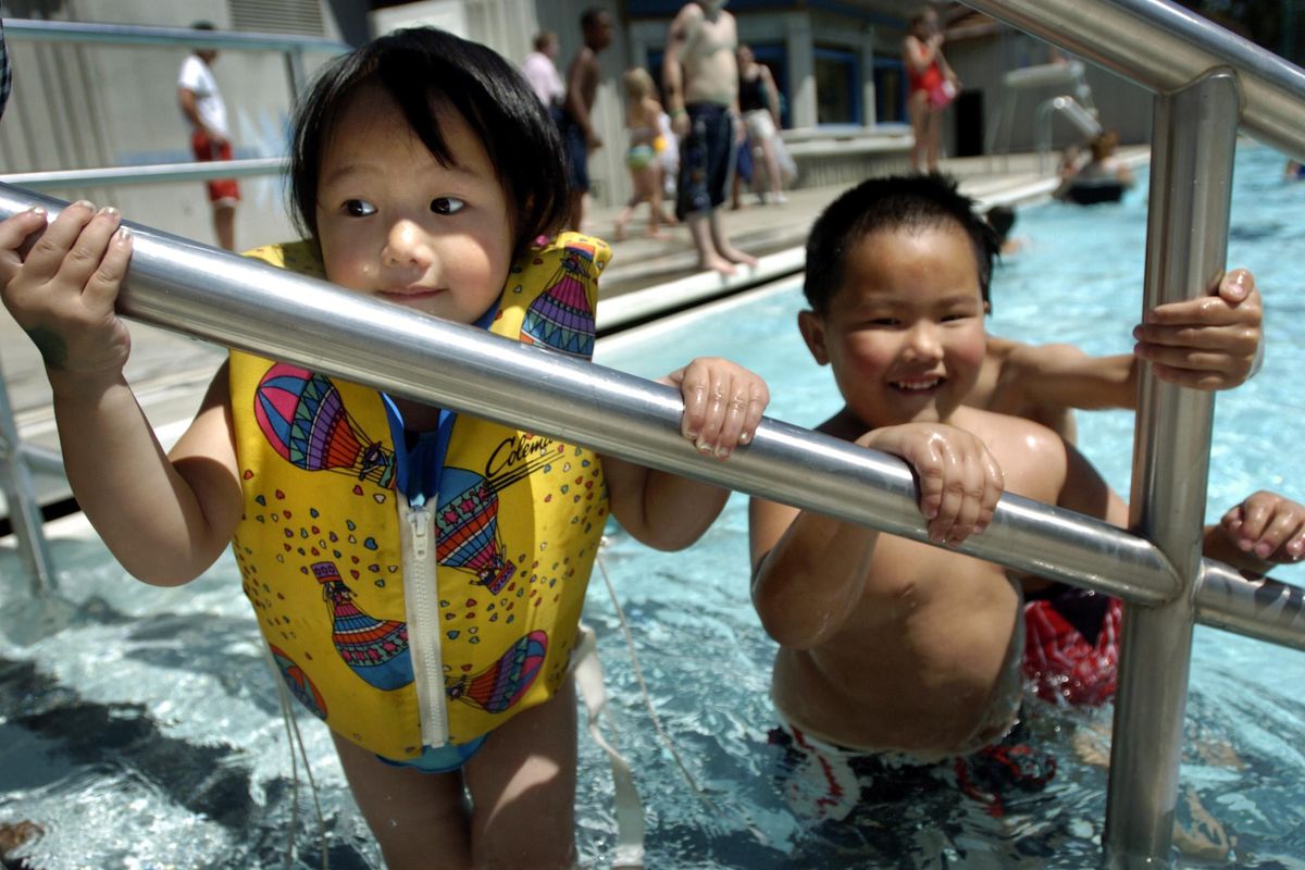 Houaha Xiong, 2, hangs on for balance while standing in the Liberty Park pool next to her mother (not pictured) and brother Simon Xiong, right, Tuesday afternoon. Voters in Liberty Lake are being asked to weigh in on a $9 million bond to fund a new community center near Town Square Park. (Holly Pickett / The Spokesman-Review)