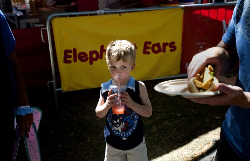 His face dashed with the remnants of a huckleberry ice cream cone, Gavin Scoggin, 5, keeps an eye on his father Sean’s Fish Po’ Boy Sandwich as he finishes off a juice drink during Spokane Pig Out in the Park on Wednesday in Riverfront Park. (Tyler Tjomsland)