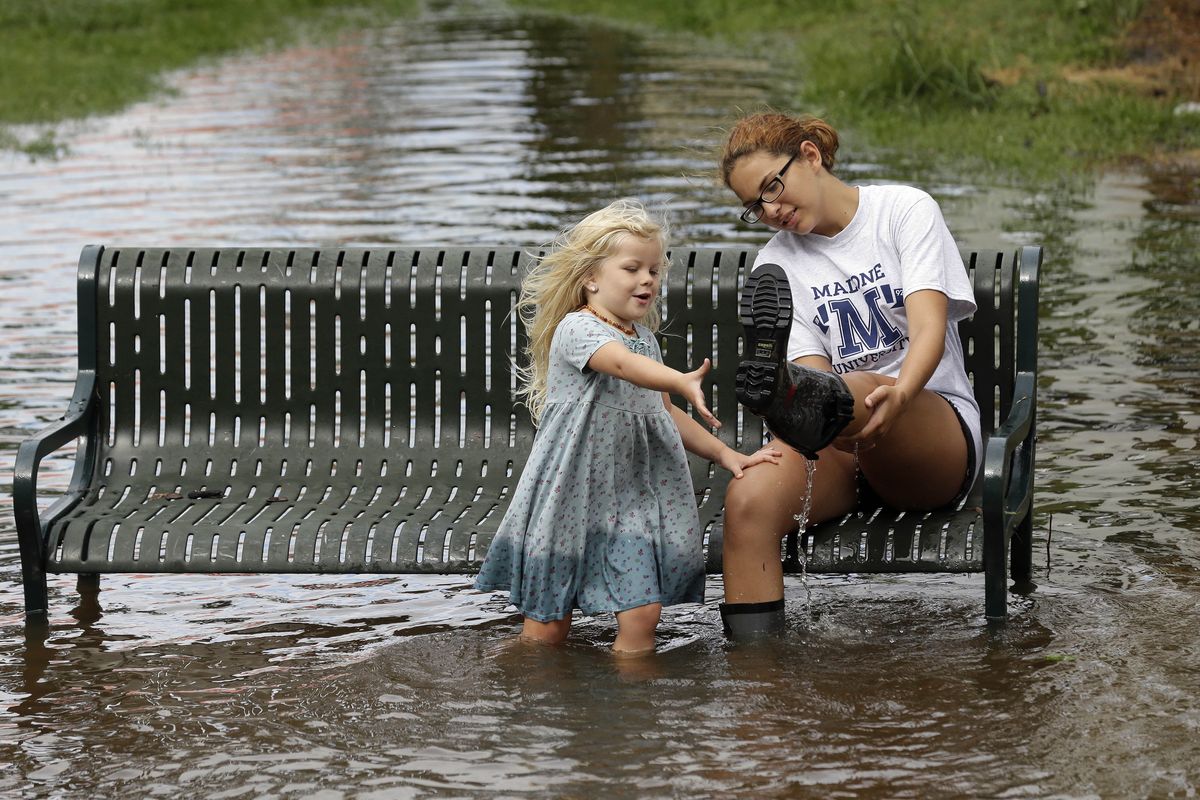 Katie Bender is assisted Friday by Johanna Bender, left, as they dump water from a boot while sitting on a flooded street after Hurricane Arthur passed through Manteo, N.C. Arthur began moving offshore and away from North Carolina’s Outer Banks earlier in the day. (Associated Press)