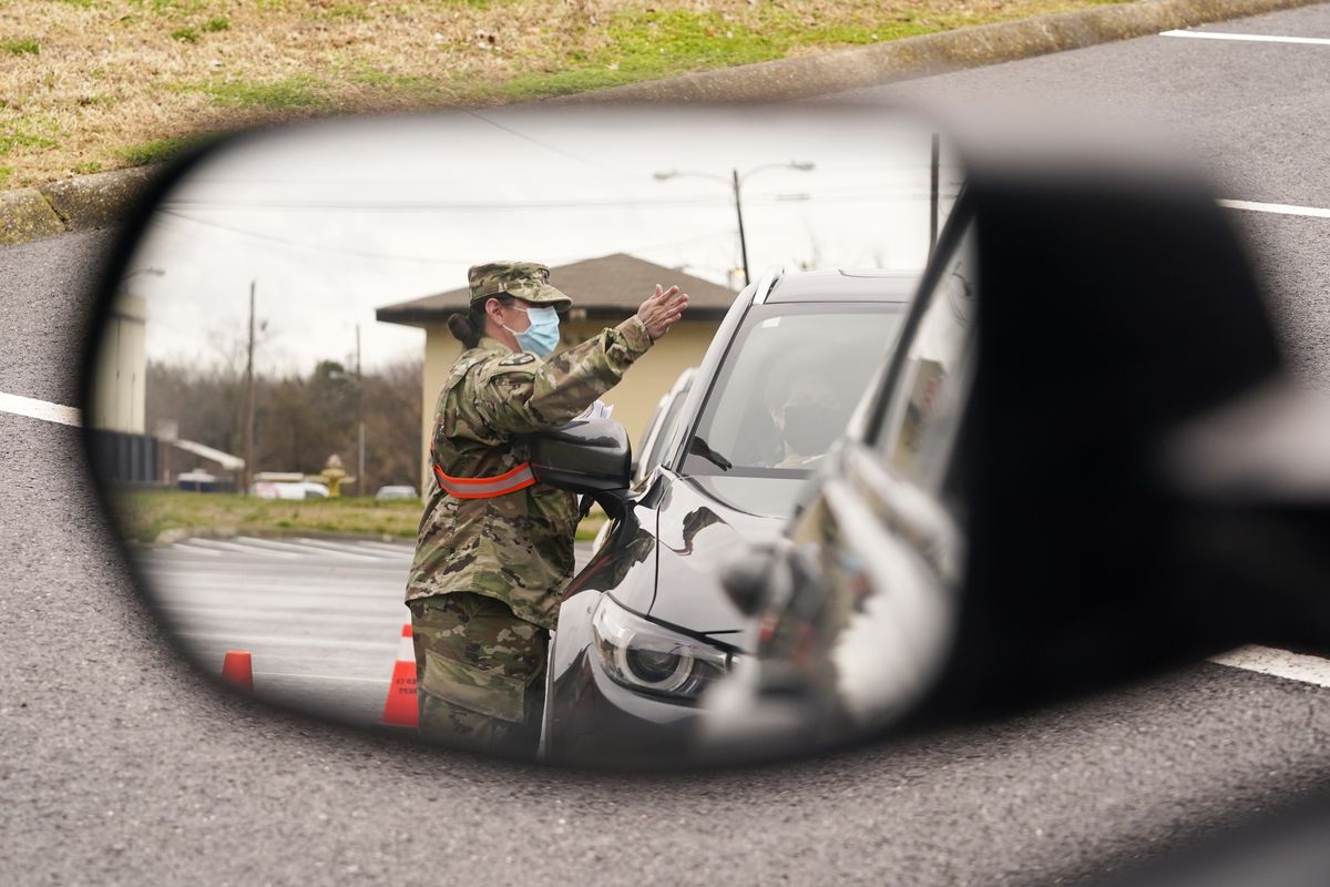 A National Guard soldier directing drivers is reflected in the mirror of a car waiting in a COVID-19 vaccination line Feb. 26, 2021, in Shelbyville, Tenn. Tennessee has continued to divvy up vaccine doses based primarily on how many people live in each county, and not on how many residents belong to eligible groups within those counties. (Mark Humphrey)