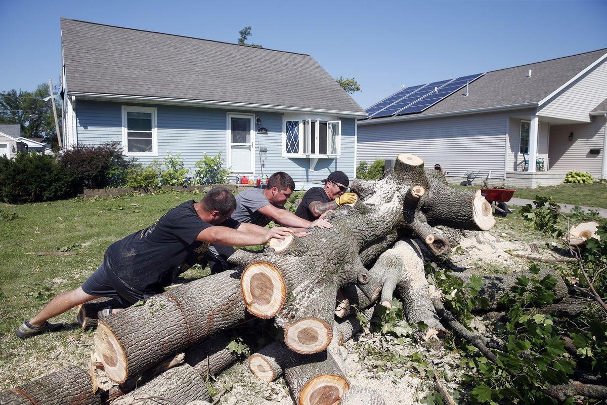 From left, Grant Whitmore, Jason Kirk and Peter Delaney roll a tree trunk while cutting it apart at Whitmore’s home in  (Associated Press)