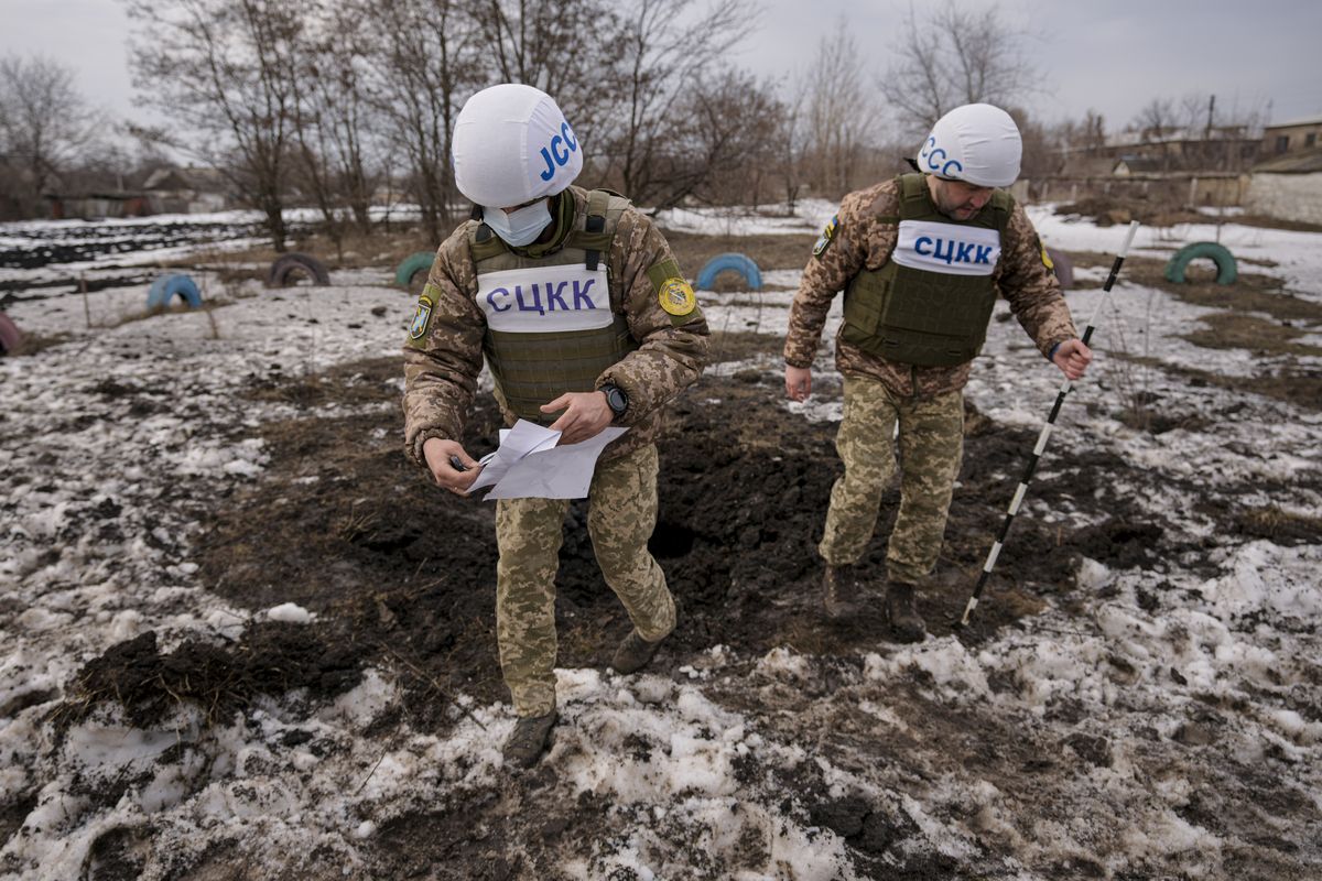 Members of the Joint Centre for Control and Coordination on ceasefire of the demarcation line, or JCCC, survey a crater from an artillery shell that landed near a school in Vrubivka, one of the at least eight that landed in the village today, according to local officials, in the Luhansk region, eastern Ukraine, Thursday, Feb. 17, 2022. U.S. President Joe Biden warned that Russia could still invade Ukraine within days and Russia expelled the No. 2 diplomat at the U.S. Embassy in Moscow, as tensions flared anew in the worst East-West standoff in decades. (Vadim Ghirda)