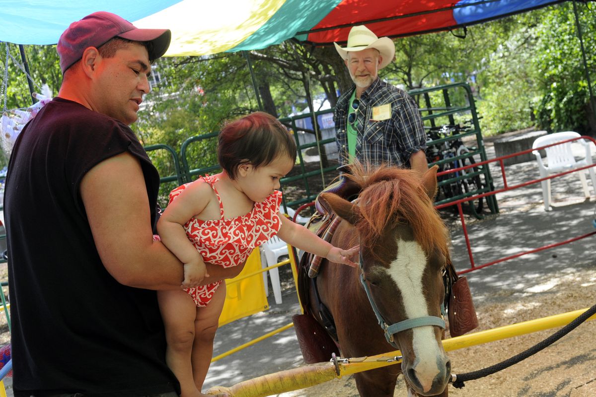 James Swan of Omak holds his grand daughter, Kloee Elsberg, as she pets her pony before riding it at Riverfront Park, Sat., June 25, 2011. Rick Perrenoud (with cowboy hat) and his wife (not pictured), Susan, own the horses and operate the ride.  J. (J. Rayniak / The Spokesman-Review)