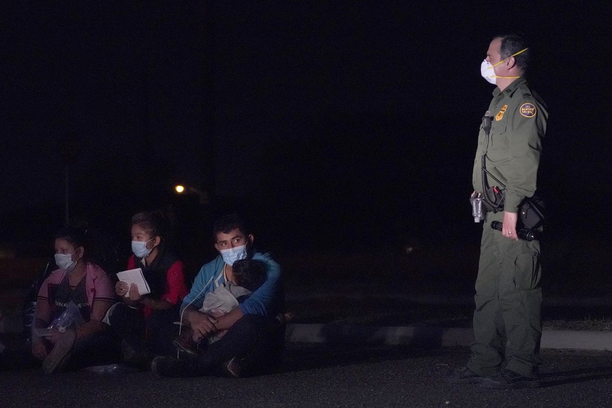 In this March 24, 2021 photo, a migrant man, center, holds a child as he looks at a U.S. Customs and Border Protection agent at an intake area after crossing the U.S.-Mexico border, early Wednesday, March 24, 2021, in Roma, Texas. The Biden administration said Monday that four families that were separated at the Mexico border during Donald Trump