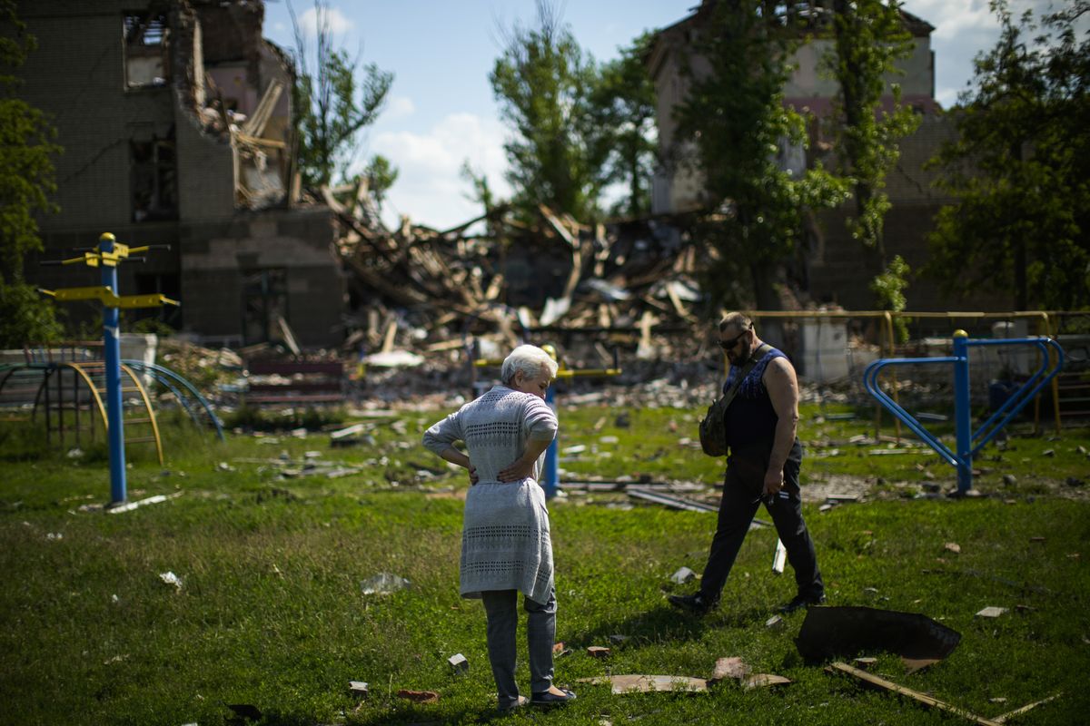 Local residents stand next to a school destroyed in a Russian bombing in Bakhmut, eastern Ukraine, Tuesday, May 24, 2022. The town of Bakhmut has been coming under increasing artillery strikes, particularly over the last week, as Russian forces try to press forward to encircle the city of Sieverodonetsk to the northeast.  (Francisco Seco)