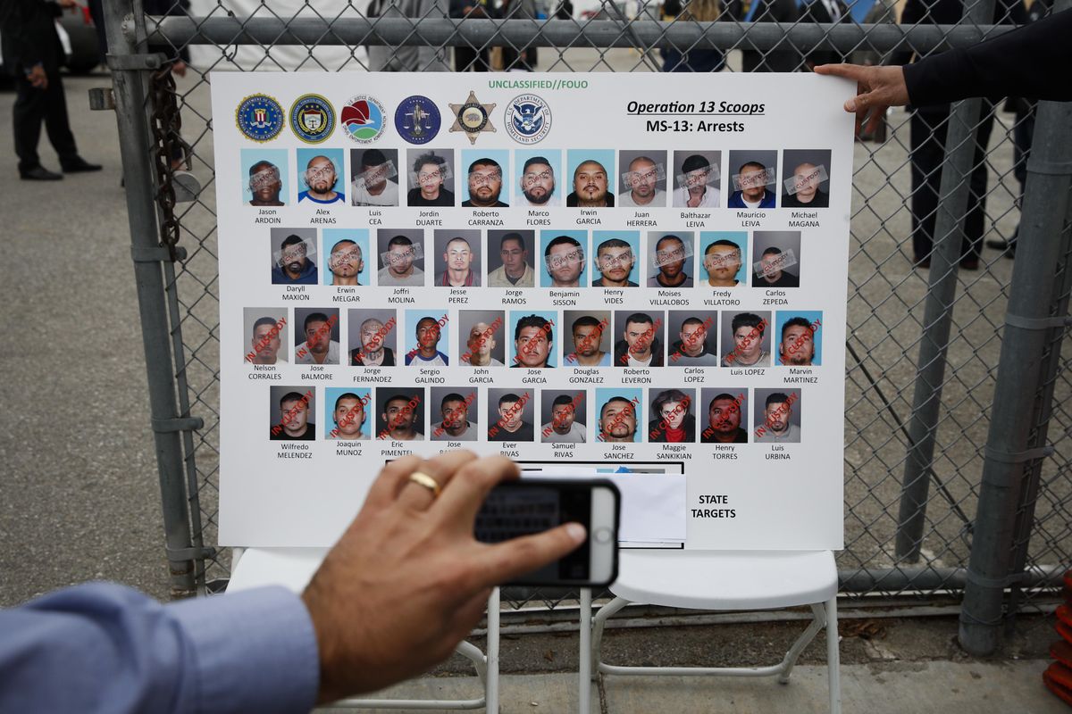 A reporter uses his smartphone to photograph a board showing images of MS-13 gang members during a news conference Wednesday, May 17, 2017, in Los Angeles. (Jae C. Hong / Associated Press)