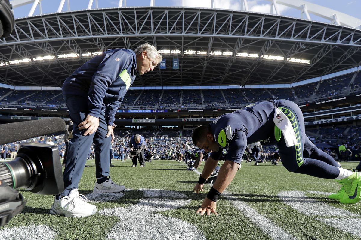 Seattle Seahawks head coach Pete Carroll, left, talks with quarterback Russell Wilson as Wilson stretches before last Sunday’s game  in Seattle. (Ted S. Warren / AP)